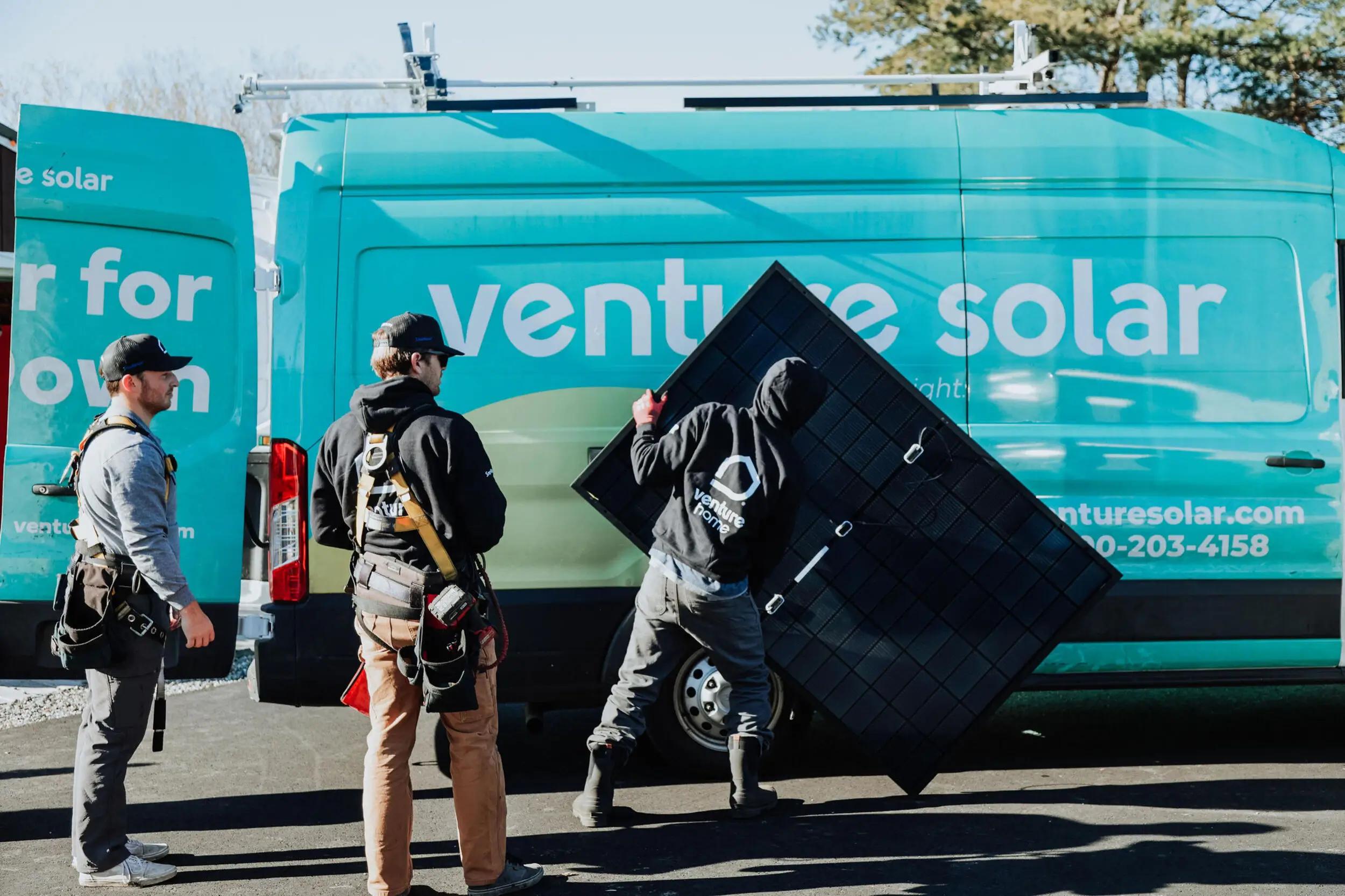 Three workers stand near a teal Venture Solar van; one carries a large black solar panel, highlighting their expertise in installing solar panels.